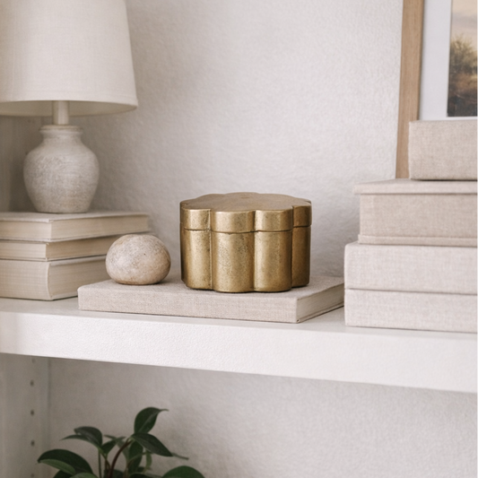 White shelf with decorative items including a lamp, books, a gold box, and a plant.