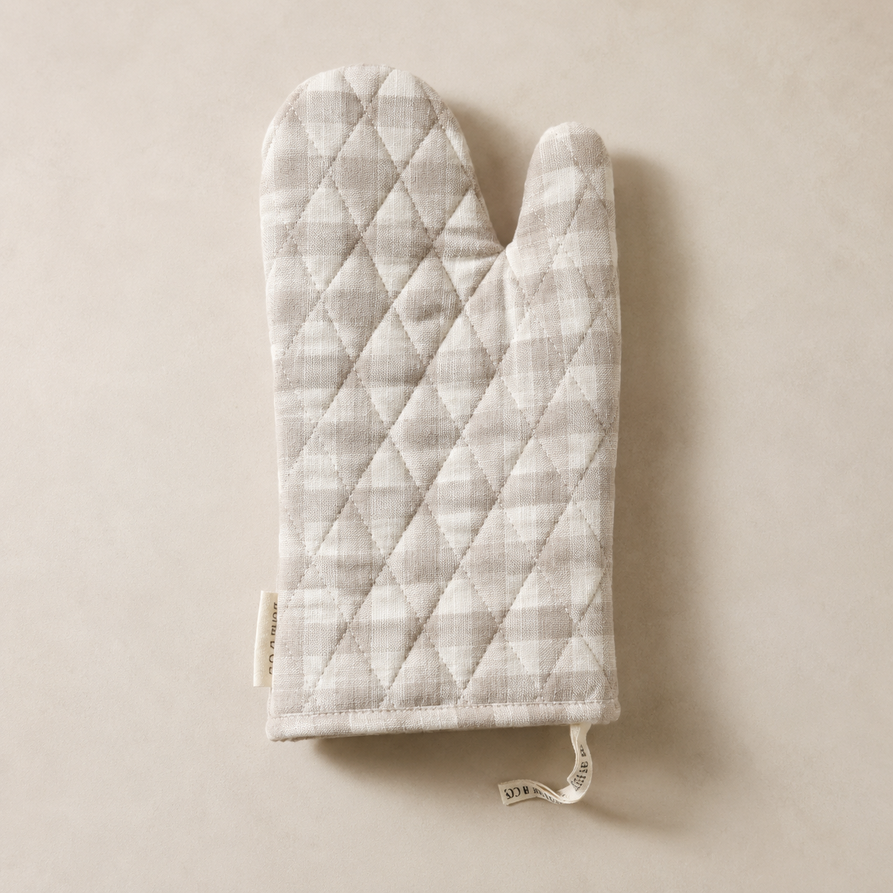 Beige gingham linen oven mitt by Luxe B Co. with quilted texture and loop for hanging, designed for heat protection in the kitchen.