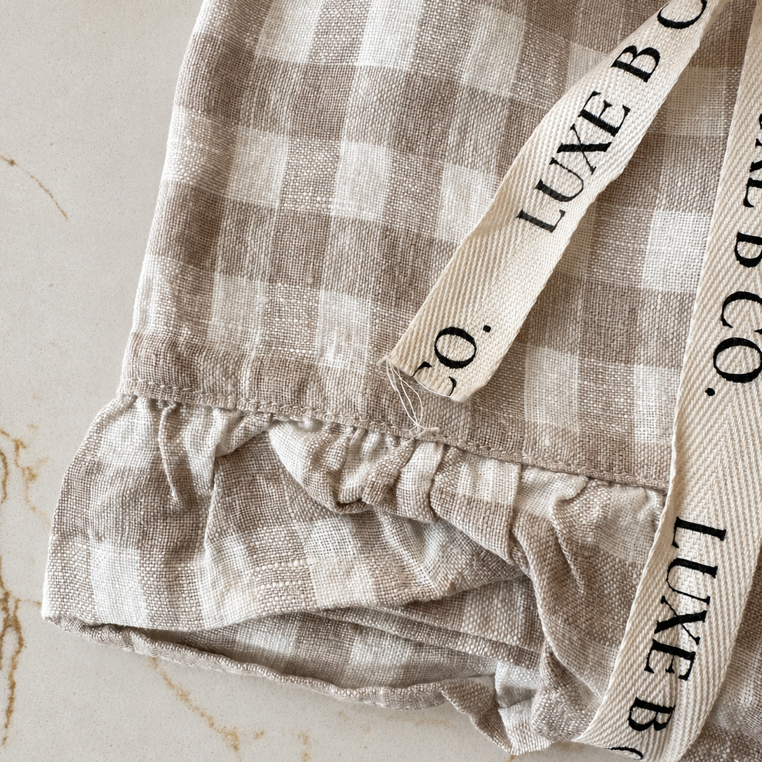 Beige gingham linen dish towel with ruffle edging from Luxe B Co, perfect for kitchen decor and drying dishes.