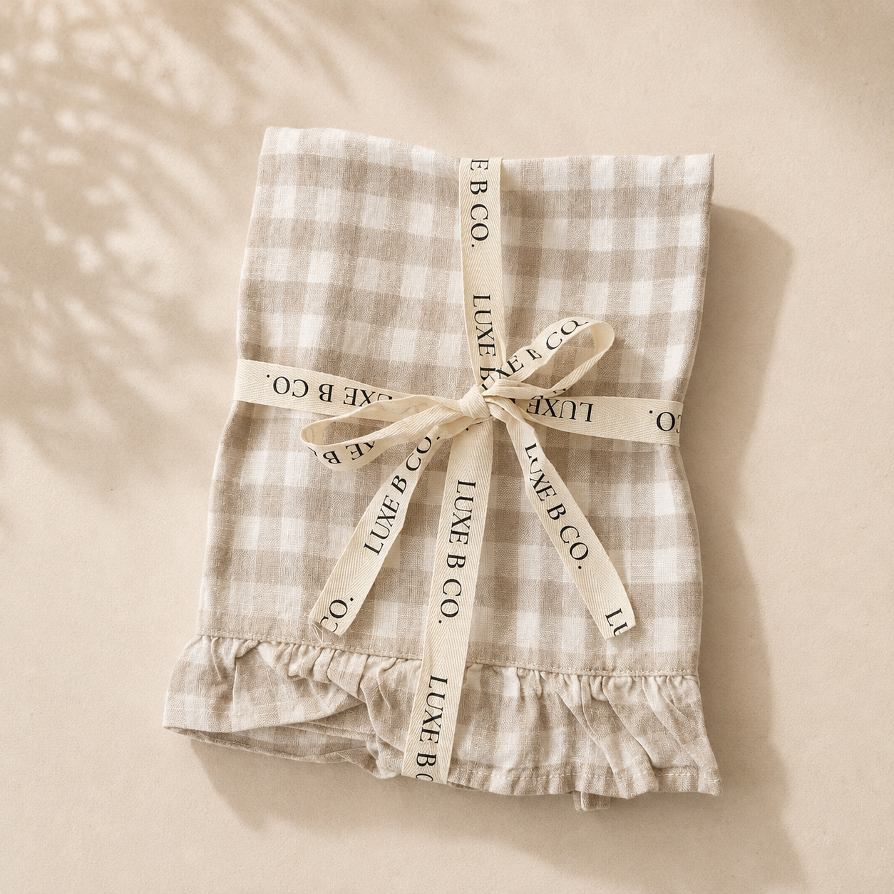 Beige gingham linen dish towel with ruffle edge by Luxe B Co, ideal for kitchen decor and drying dishes.