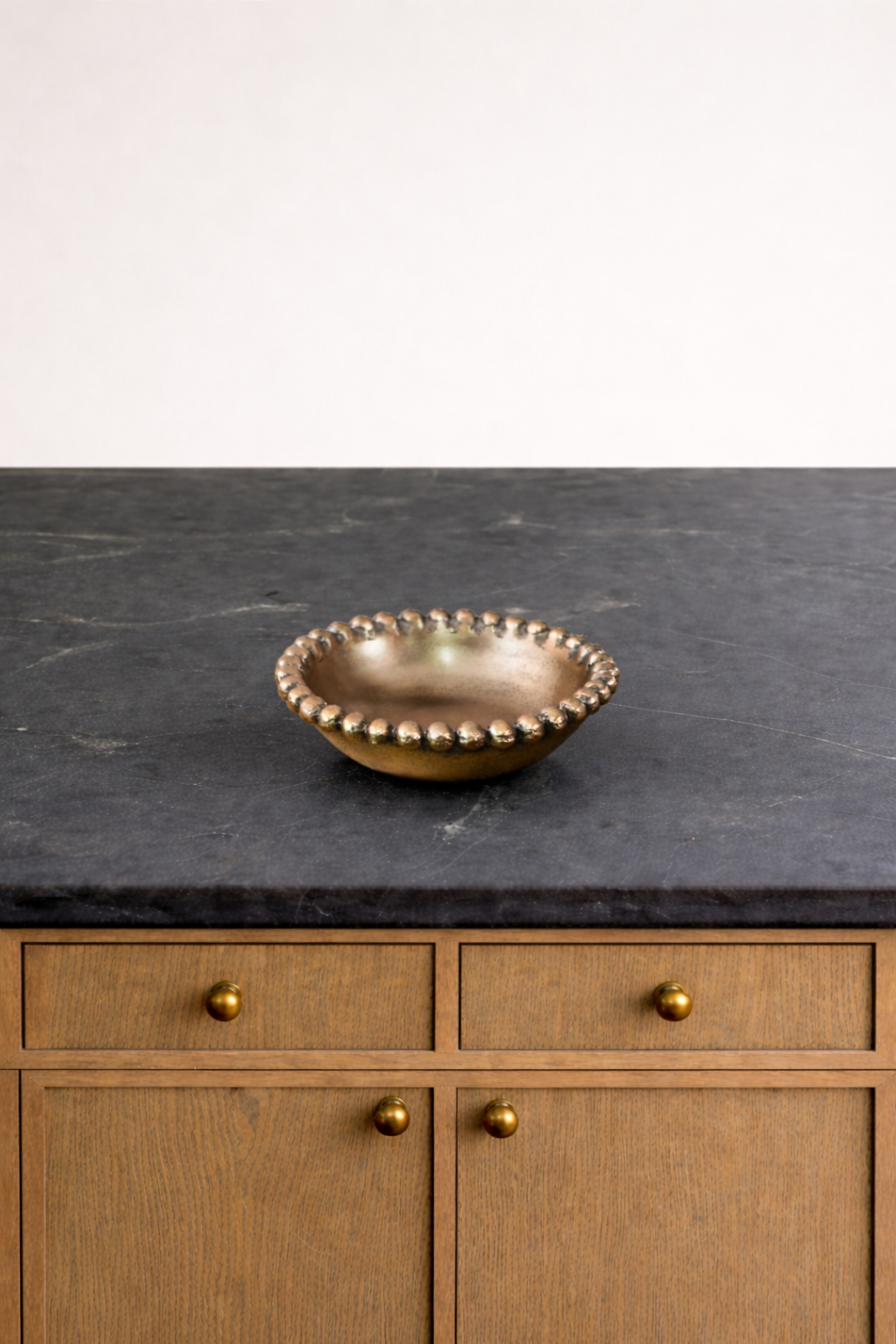 Bronze bowl on a dark countertop with wooden cabinets in the background