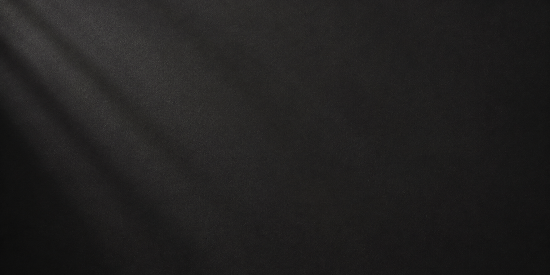 A close-up of a dark black textured surface with soft diagonal light streaks across it.