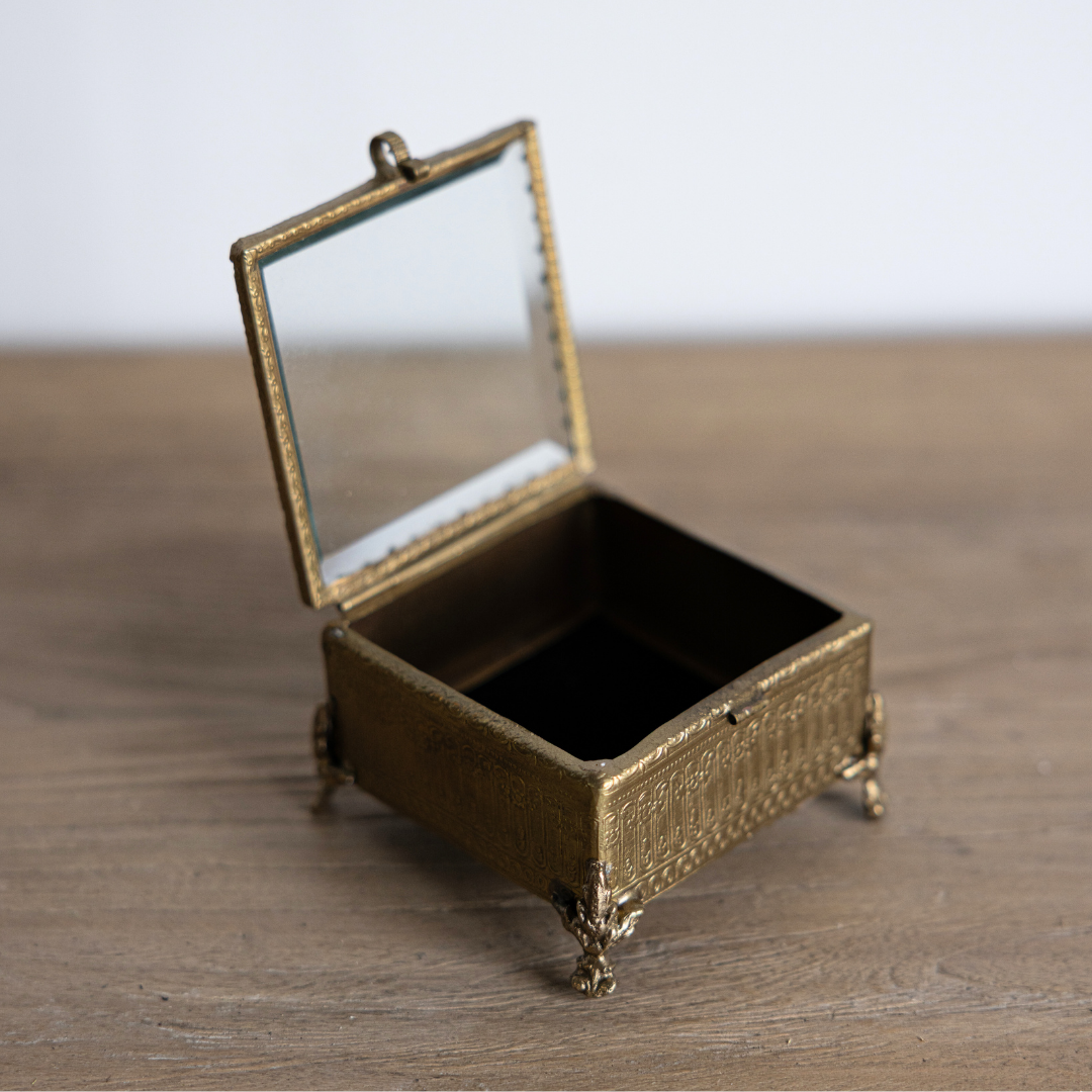 Decorative brass and glass box with a footed beveled design by Luxe B Co, ideal for stylish home decor or jewelry storage.