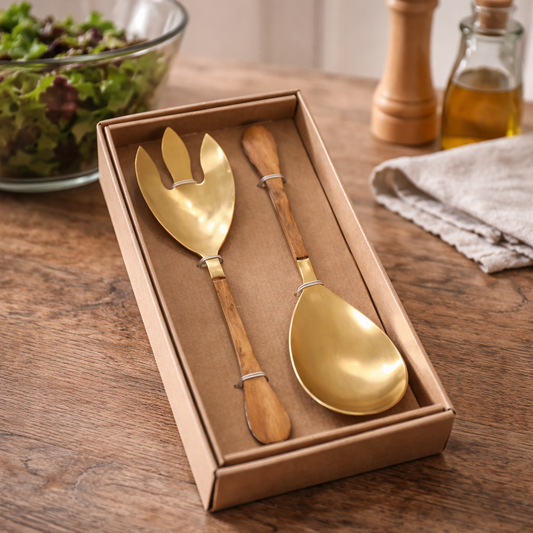 Gold salad servers in a box on a wooden table with a salad in the background