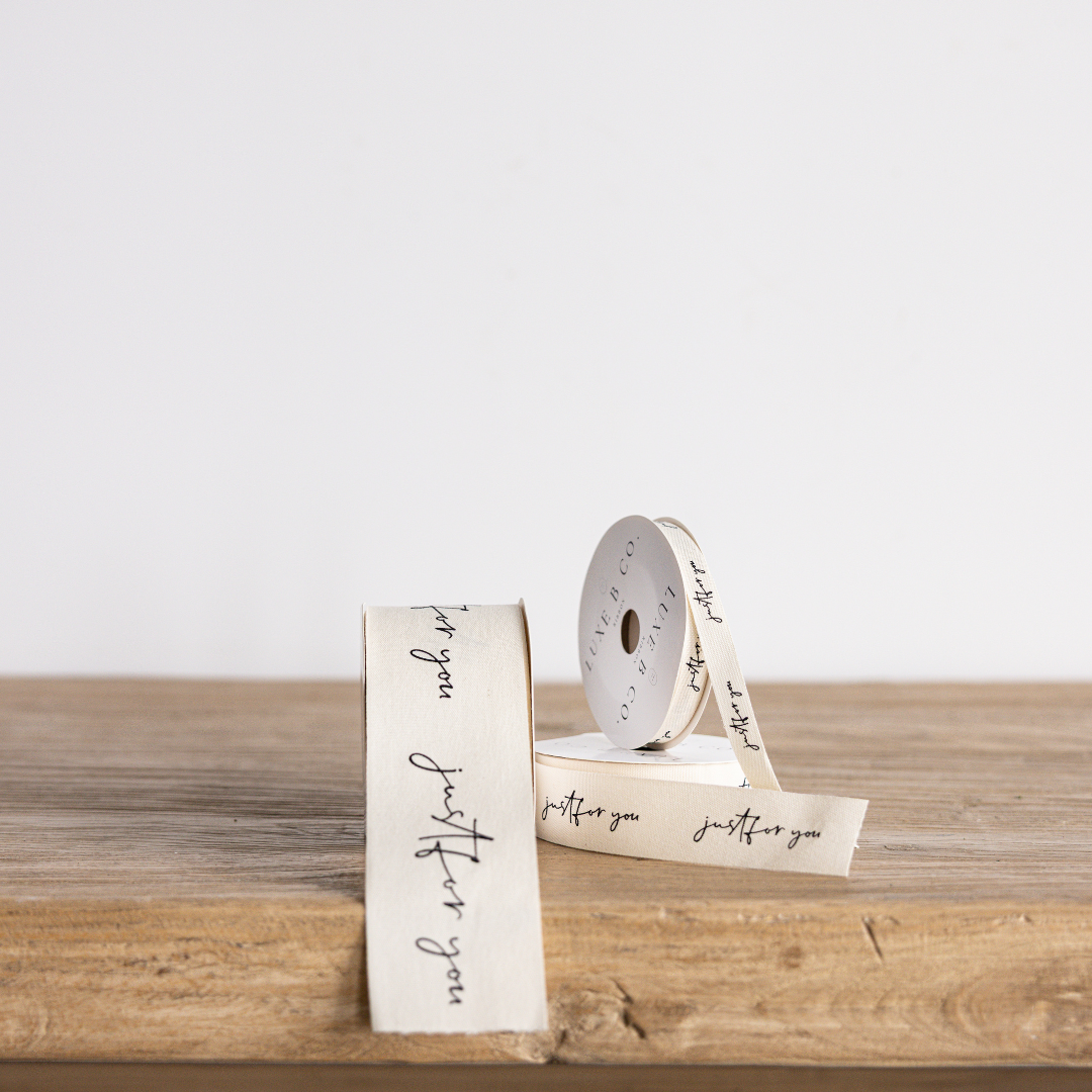 Cursive "Love You More" ribbon by Luxe B Co Wholesale, featuring elegant handwritten style on a satin ribbon.