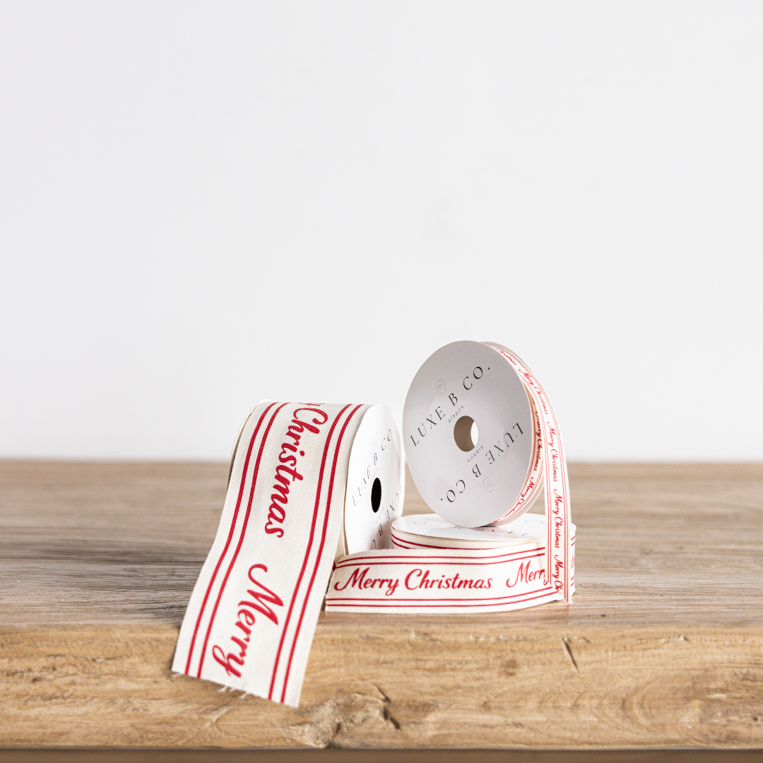 Red cursive writing Merry Christmas ribbon by Luxe B Co Wholesale, featuring festive holiday design and vibrant red color.