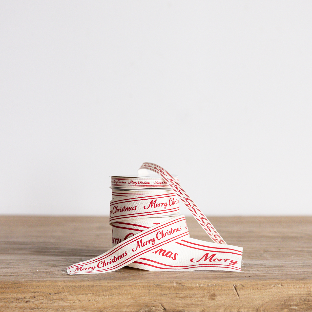 Red cursive Merry Christmas ribbon by Luxe B Co Wholesale, featuring festive holiday script on glossy red satin fabric.