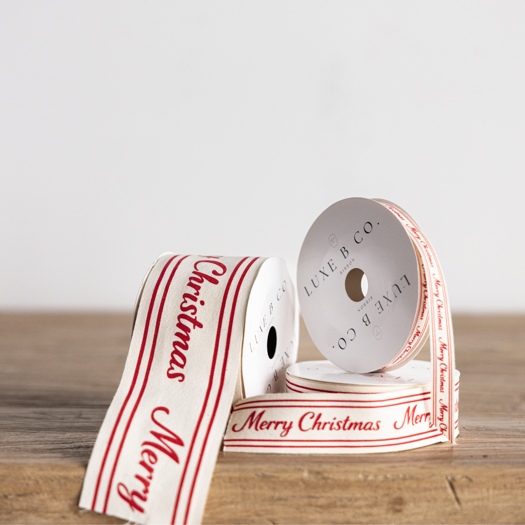 Red cursive Merry Christmas ribbon by Luxe B Co Wholesale, featuring festive holiday lettering and decorative red design.