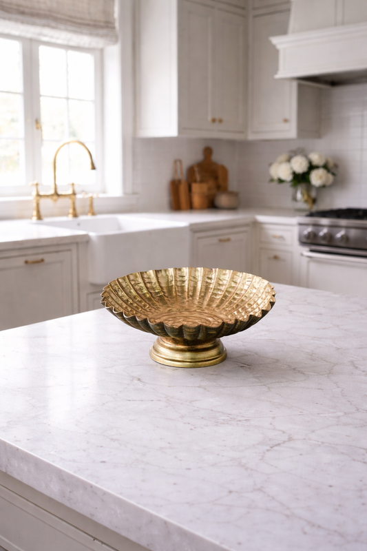 Gold decorative bowl on a marble kitchen countertop with white cabinets and appliances in the background.