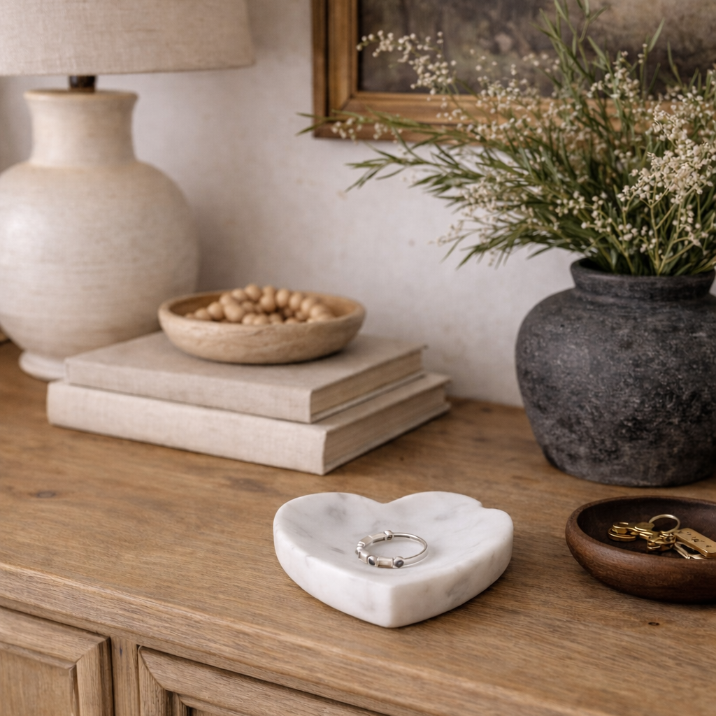 Decorative items on a wooden surface including a lamp, books, a vase with flowers, and a heart-shaped dish.